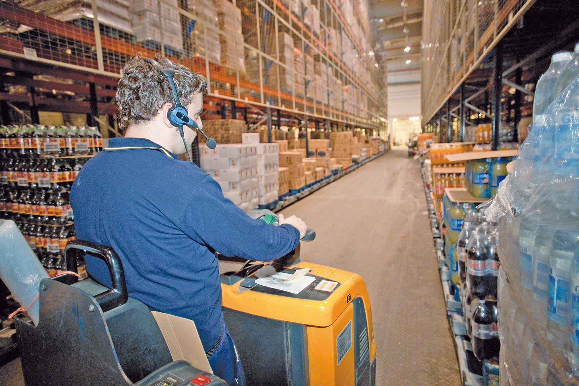 Een magazijnmedewerker zet bestellingen in dozen klaar, daarbij ondersteund door een voicepicking systeem Een magazijnmedewerker zet bestellingen in dozen klaar, daarbij ondersteund door een voicepicking systeem